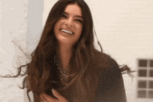 a woman with long brown hair is smiling and holding her chest
