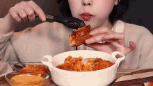 a woman is eating a slice of pizza from a bowl with tongs