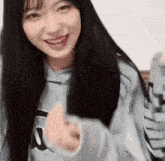 a young woman with long black hair is wearing a kappa sweatshirt and giving a thumbs up .