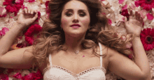a woman in a white lace top is laying in a bed of flowers