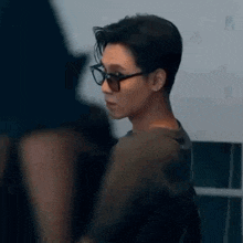 a man wearing glasses and a black shirt is standing in front of a mirror .