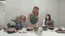 three women are standing around a table with potted plants and a bag that says " twice " on it