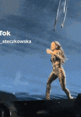 a woman is dancing on a stage with a blue sky behind her and the words tok steczkowska