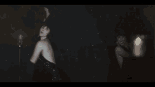 a woman in a black dress stands in front of a microphone in a dark room