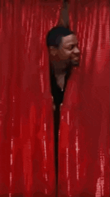 a man in a suit is standing in front of a red curtain and smiling