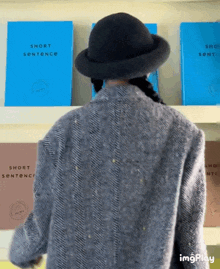 a woman wearing a hat stands in front of a shelf of short sentences books