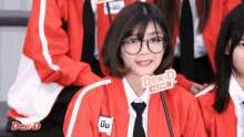 a girl wearing glasses and a red jacket has a dek-d live sign on her jacket