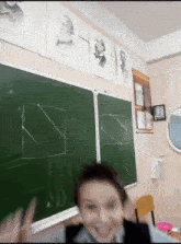 a boy stands in front of a chalkboard in a classroom