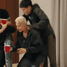 a man in a black hoodie is being piggybacked by two other men holding red cups