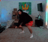 a man in a black hoodie and red shorts is dancing in front of a painting that says king