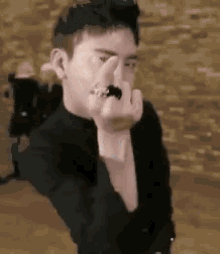 a man in a black suit is covering his face with his hand .