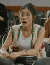 a woman is sitting in a classroom wearing a sweater vest and a white shirt