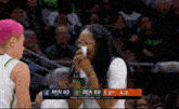 a woman wipes her nose during a basketball game with the scoreboard showing sea 68 to min 65
