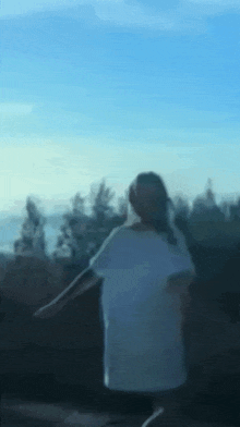 a blurry picture of a woman in a white shirt standing in front of a blue sky