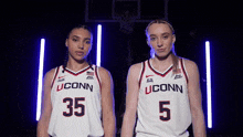 two female basketball players wearing uconn uniforms stand next to each other