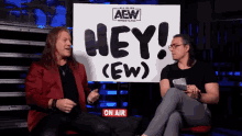 two men sitting in front of a sign that says hey