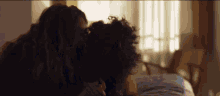 a couple of women are kissing on a bed in a room .
