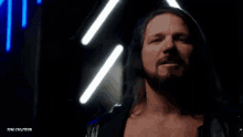 a wrestler with long hair and a beard is standing in front of a neon sign .