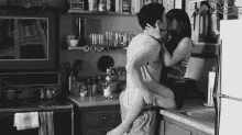 a man is carrying a woman on his lap and kissing her in a kitchen .