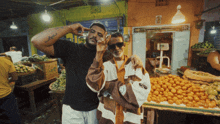 a man with a tattoo on his arm stands next to another man in front of a fruit stand