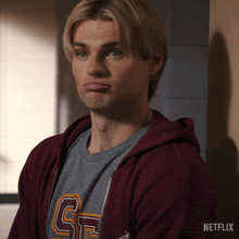 a man wearing a maroon hoodie and a grey t-shirt with the letter g on the front