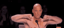 a man without a shirt is flexing his muscles in front of a microphone .