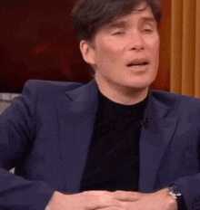 a man in a suit and black shirt is making a funny face while sitting down .