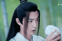 a young man with long hair is holding a small white rabbit in his hands .