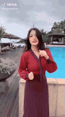 a woman in a red top and purple skirt is dancing in front of a swimming pool ..