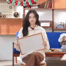 a young woman is sitting on a couch holding a white board .