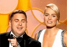 a man in a tuxedo and a woman in a white dress are standing next to each other on a stage .
