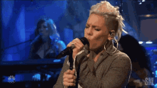 a woman singing into a microphone with the letters sns on the bottom