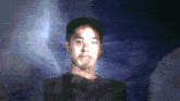 a man in a black shirt is standing in front of a dark brick wall