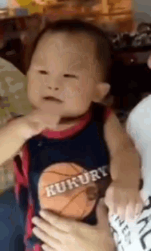 a baby wearing a kukury basketball shirt is being held