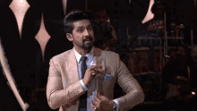a man in a tan suit and tie is standing in front of a drum set