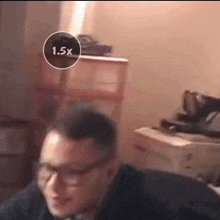 a man wearing glasses is sitting in front of a dresser with a 1.5x circle around his head