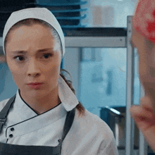a woman in a chef 's uniform is looking at another woman in a kitchen