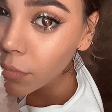 a close up of a woman 's face with a white shirt and earrings