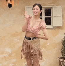 a woman in a crop top and fringed skirt stands in front of a building