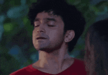 a man in a red shirt is standing next to a woman with his eyes closed and his mouth open .