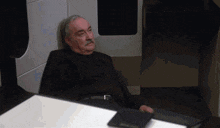 a man with a mustache is sitting on the floor in a room
