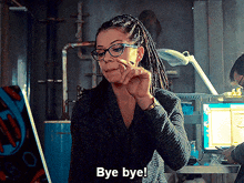 a woman with dreadlocks and glasses is saying bye bye in front of a computer .