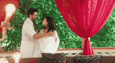 a man and a woman are dancing in front of a red curtain in a room .