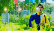 a man in a yellow and blue jacket is standing in a park with flags in the background .