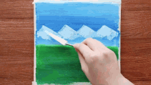 a person is using a spatula to paint a picture of mountains