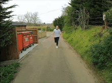 a person running down a road next to a red dumpster that says ' waste management ' on it