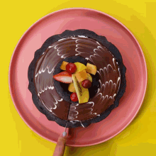 a person is cutting a chocolate cake with fruit on it