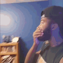 a man with a beard wearing a hat is sitting in front of a bookshelf