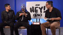 a man in a mask sits in front of a sign that says hey
