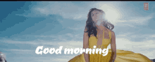 a woman in a yellow dress stands in front of a blue sky with the words " good morning " on the bottom